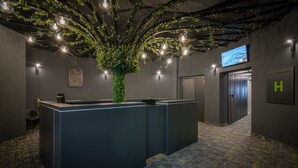 Zona de recepción con mostrador, un árbol artificial grande y una pantalla de televisión.