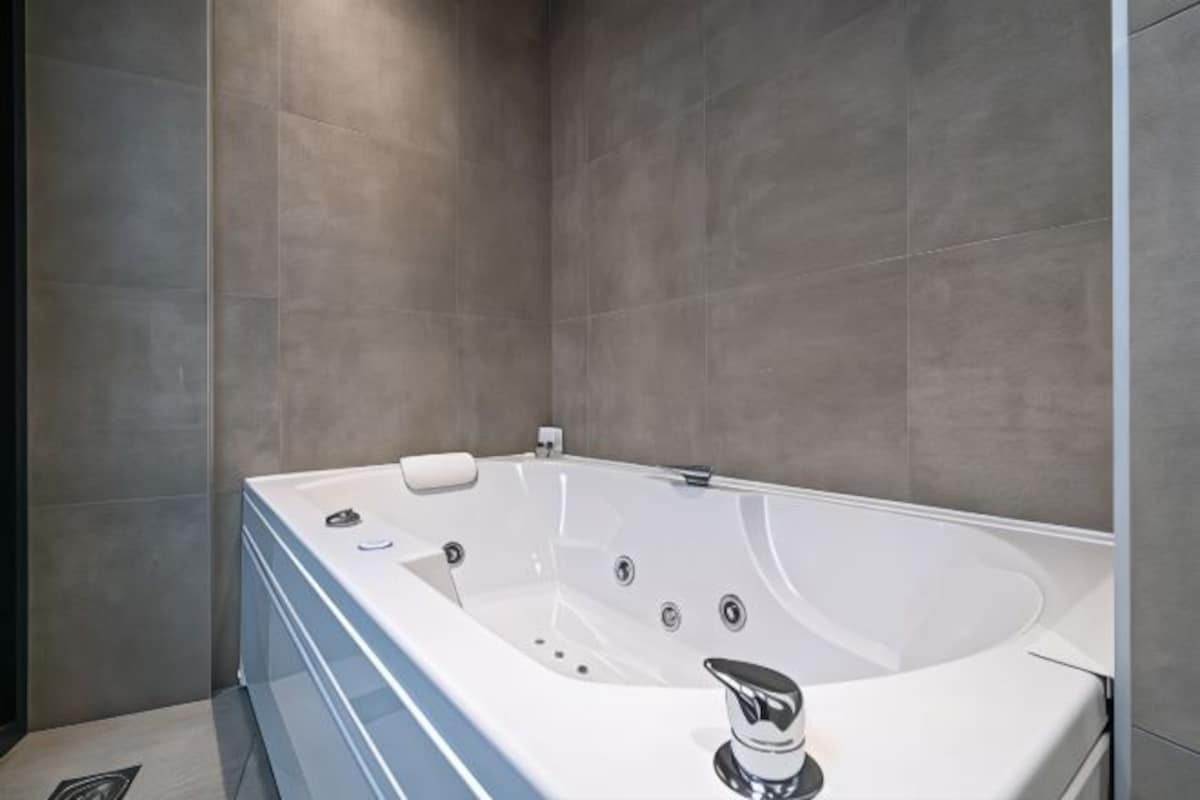 A modern bathroom with a large white bathtub, a built-in shower, and a sleek, minimalist design.