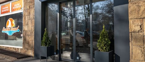 A modern building entrance with a glass door, stone facade, and two potted plants.