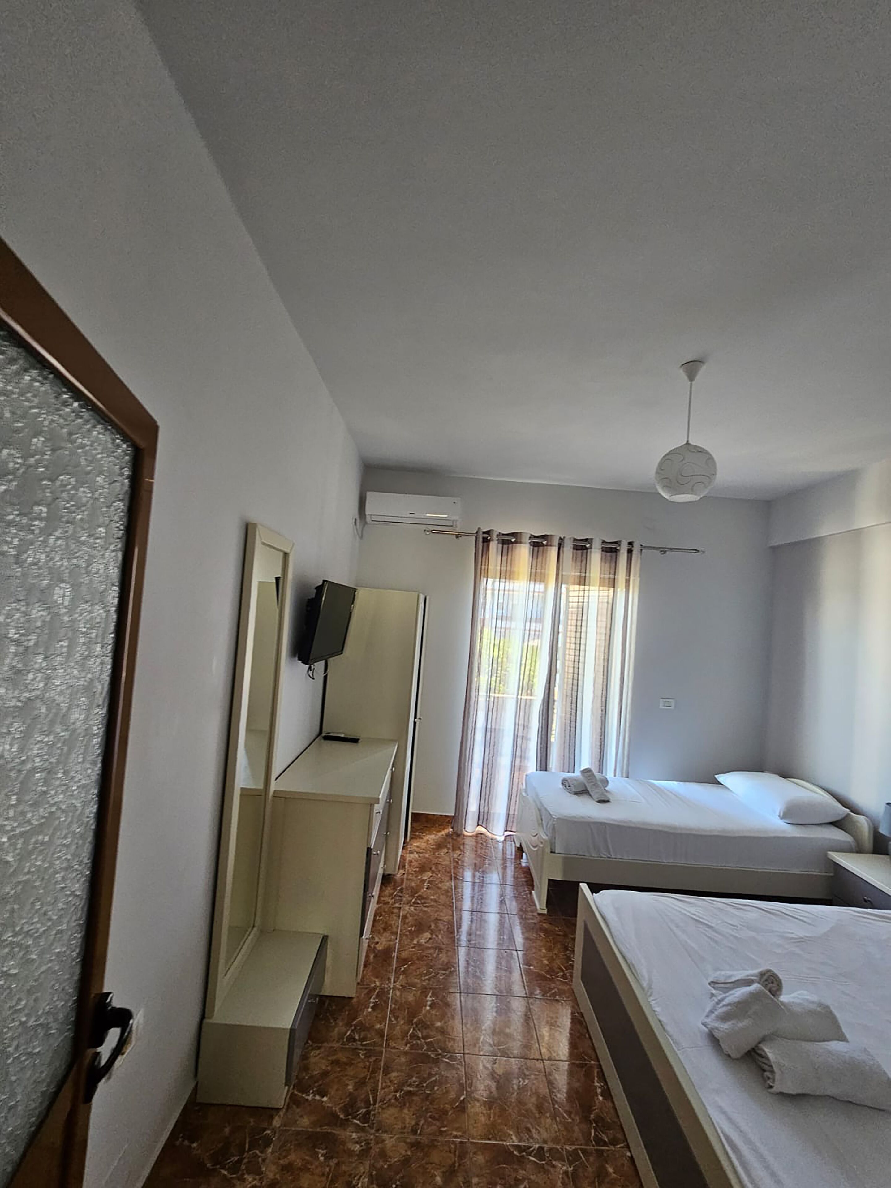 A hotel room with a bed, a desk, a TV, and a window with curtains.