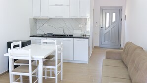 Une cuisine compacte avec des meubles blancs, un pare-feu en marbre et un coin repas comprenant une table et des chaises blanches.