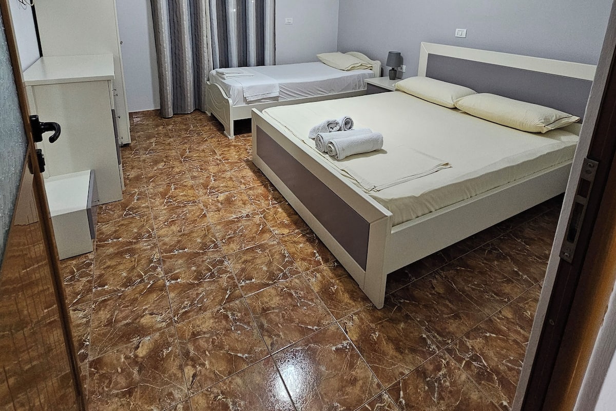 A bedroom with a bed, a desk, a chair, a TV, and a bathroom with a shower curtain.