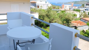 Un balcon avec une table et des chaises blanches, offrant une vue sur la mer et les bâtiments environnants.