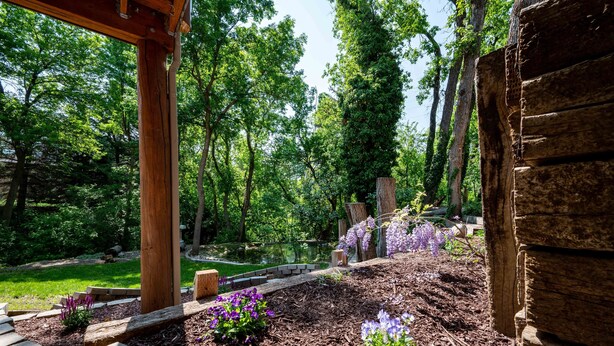 A wooden pergola with a stone pathway leading to a pond surrounded by lush greenery and purple flowers. - Mountain Haus (Ogden)