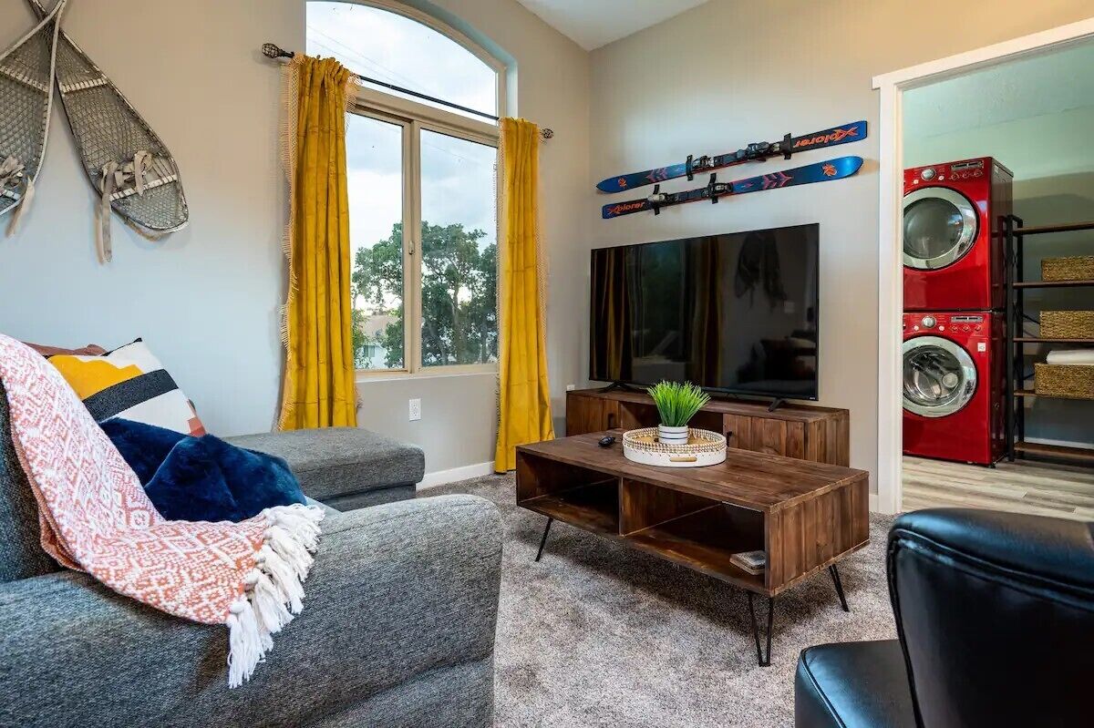 A living room with a sofa, a coffee table, a TV, and a window with curtains.
