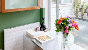 A room with a radiator, a small table with a vase of flowers, and a framed artwork on the wall. - Cosy 1bedroom Flat - 2 Min Walk to Kensington Gardens! (London)