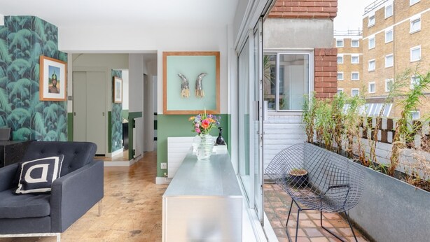 A modern living room with a sofa, a coffee table with a vase of flowers, and a dining area with a white cabinet and framed artwork. - Cosy 1bedroom Flat - 2 Min Walk to Kensington Gardens! (London)