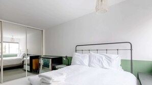 A hotel room with a bed, a desk, a chair, a mirror, and a hanging light fixture. - Cosy 1bedroom Flat - 2 Min Walk to Kensington Gardens! (London)
