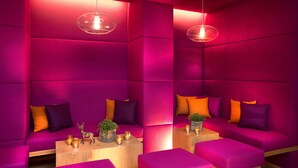 A modern room with vibrant pink walls, a wooden bench, and a small table with candles and a plant. - Hapimag Ferienwohnungen Zell am See (Maishofen)