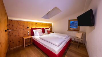 Ein Hotelzimmer mit einem hölzernen Kopfteil, einem Bett mit weißer Bettwäsche, einem Nachttisch, einem Sessel, einem an der Wand befestigten Fernseher und einem Oberlicht.