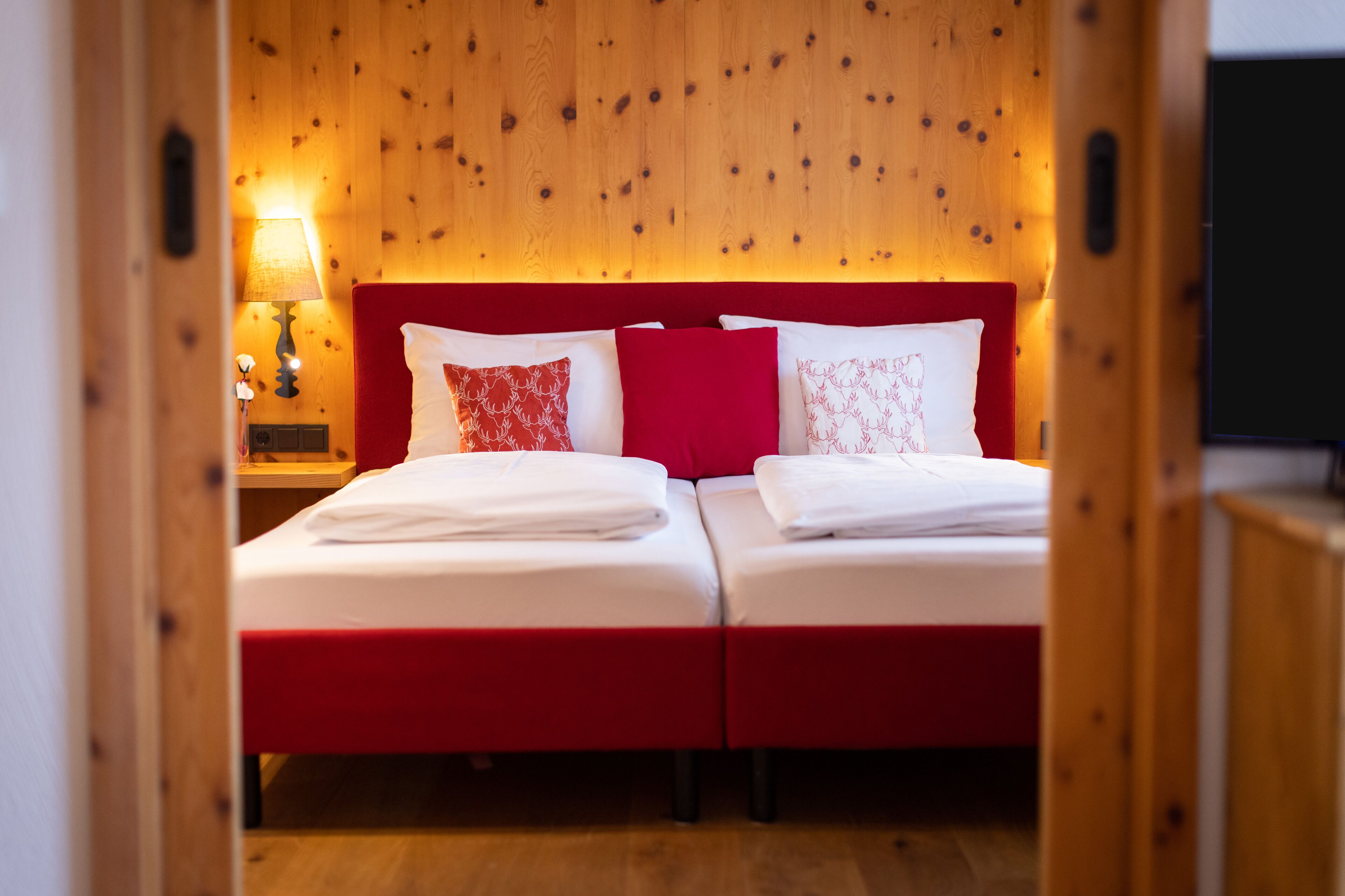 Une chambre double avec deux lits, chacun doté d’une literie rouge et blanche et d’une tête de lit en bois.
