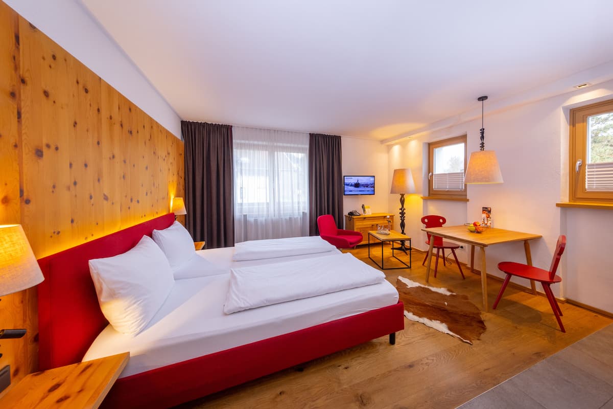 A hotel room with a large bed, a desk, two chairs, a television, and a wooden headboard.