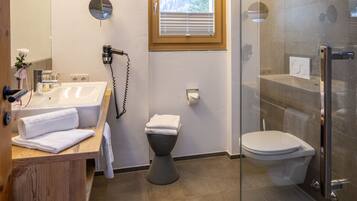 Un baño moderno con cabina de ducha de vidrio, tocador de madera, inodoro y ventana que deja entrar luz natural.