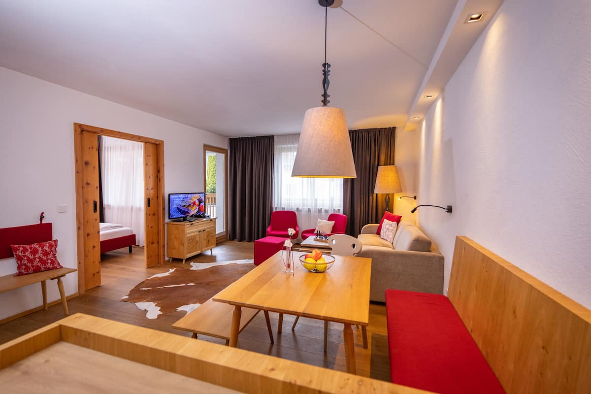 A modern living room with a wooden dining table, red and grey sofas, a TV, and a wooden cabinet.