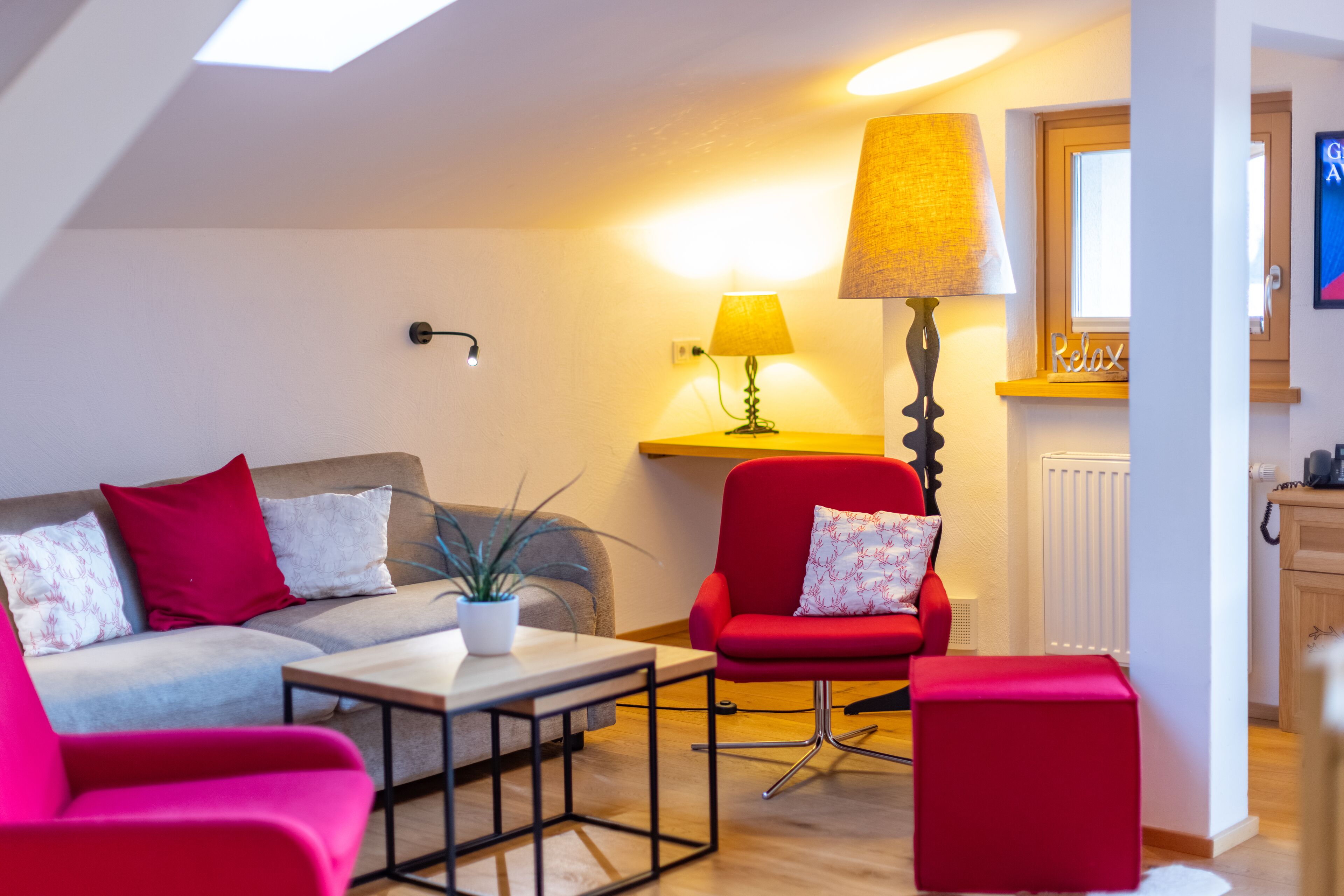 Een moderne woonkamer met een bank, een rode fauteuil, een bijzettafeltje en een lamp.