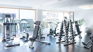 A modern gym with various exercise equipment, large windows, and a view of the city. - Hapimag Ferienwohnungen Zell am See (Maishofen)