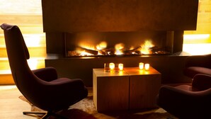 A modern living room with a fireplace, two armchairs, and a small wooden table with candles. - Hapimag Ferienwohnungen Zell am See (Maishofen)