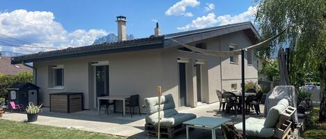 A modern house with a patio area featuring outdoor furniture, a covered table, and a barbecue grill.