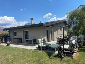 Une maison moderne dotée d’un patio aménagé avec des meubles d’extérieur, une table couverte et un barbecue.