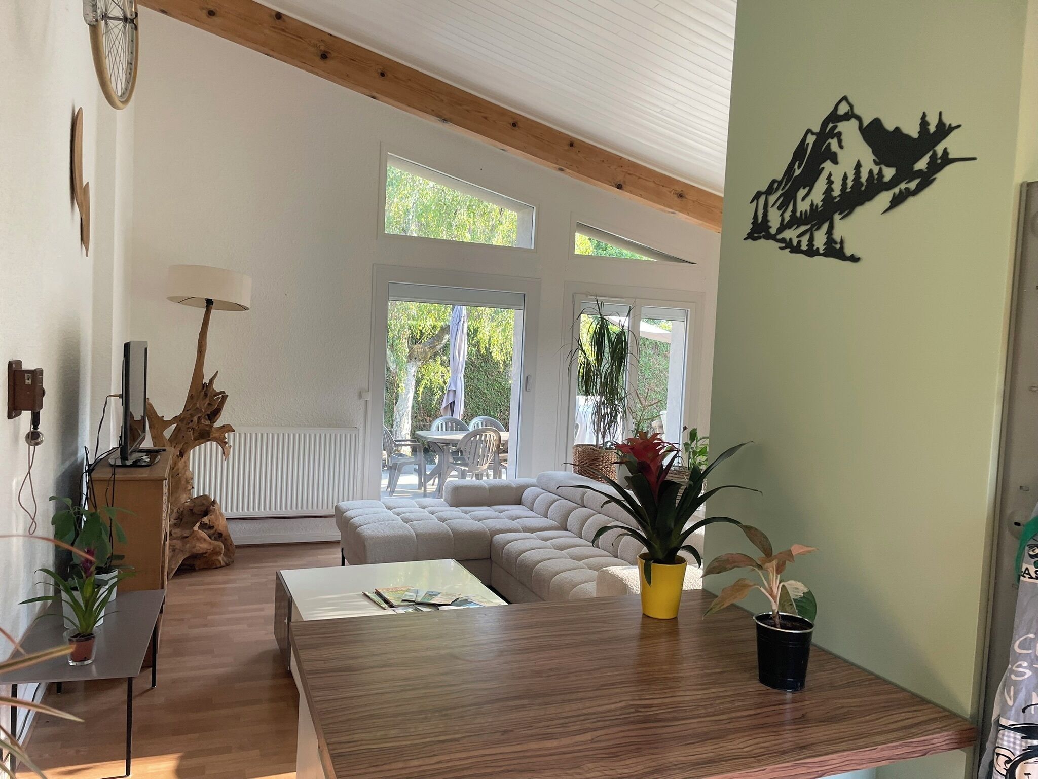 A spacious living room with a wooden floor, a large sofa, a dining table, and a view of the outdoors through large windows.