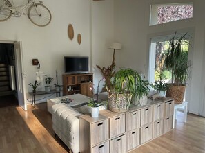 A modern living room with a sofa, coffee table, TV, and various potted plants. - Maison familiale proche du lac d'Annecy, espace vert et tranquillité. (Saint-Jorioz)