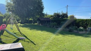 Een gazon met een schommel, een tuinhuisje en een omheining.