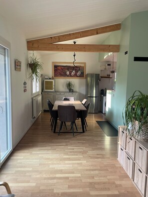 A modern kitchen with wooden beams, a dining table with chairs, and a refrigerator. - Maison familiale proche du lac d'Annecy, espace vert et tranquillité. (Saint-Jorioz)