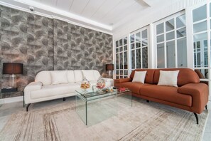 Un salon avec deux canapés, une table basse en verre et un mur orné d’un motif.