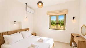 Ein Schlafzimmer mit Bett, Nachttischen, einem Schreibtisch, einem Spiegel und einem Fenster mit Blick auf Bäume.