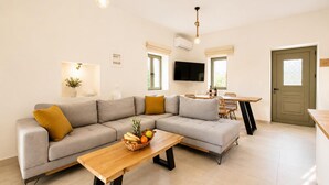 Ein modernes Wohnzimmer mit einer Eckcouch, einem Holztisch, einer Essecke mit Tisch und Stühlen sowie einem an der Wand befestigten Fernseher.