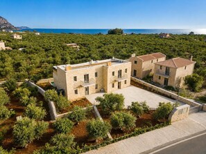 Un edificio de piedra con techo plano, rodeado de vegetación y una vista despejada del mar.