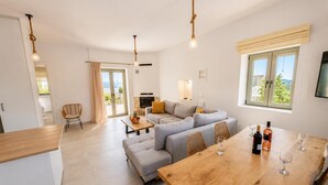 Ein modernes Wohnzimmer mit einer Couch, einem Esstisch mit Weingläsern und einem an der Wand befestigten Fernseher.