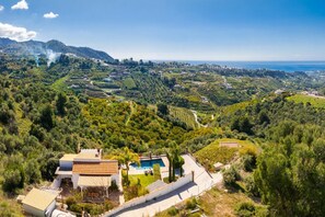 A villa with a swimming pool, surrounded by lush greenery and hills.