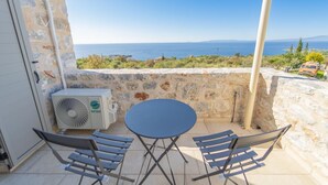 A balcony with a table and chairs, an air conditioning unit, and a stone wall overlooking a scenic view.