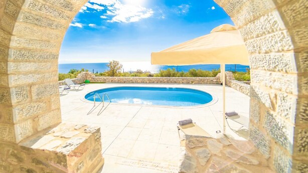 A stone archway framing a swimming pool with a view of the sea.