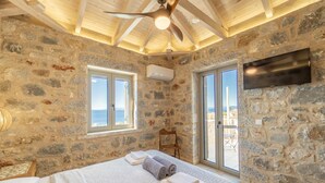 A stone-walled bedroom with a bed, a ceiling fan, and a TV mounted on the wall.