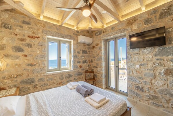 Ein Schlafzimmer mit Steinwänden, einem Bett, einem Deckenventilator und einem an der Wand montierten Fernseher.