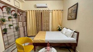 Une chambre à coucher comprenant un lit, une chaise, une petite table, un ventilateur de plafond et un climatiseur fixé au mur.