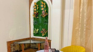 Un coin salon avec une table ronde et une chaise jaune, un mur décoratif orné d’un motif de feuilles vertes et un meuble en bois.
