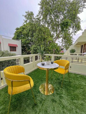 A rooftop terrace with two yellow chairs and a small table, surrounded by green artificial grass and a large tree. - Serene Stay 5bhk Luxury Villa Varanasi (Varanasi)
