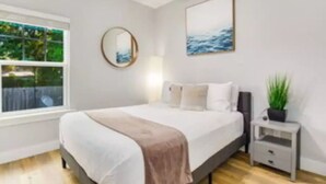 Un dormitorio con cama, mesita de noche, espejo y ventana con vistas a zonas verdes.