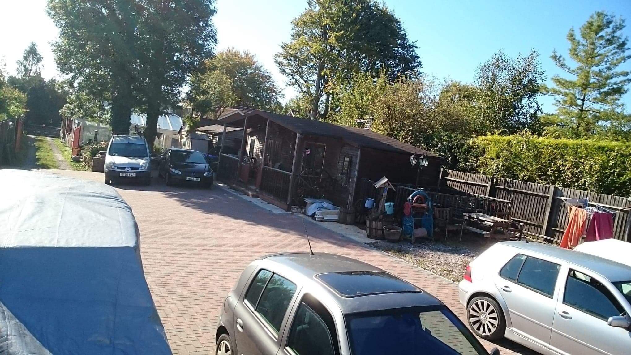 A parking area with several cars, a small building with a sloped roof, and a wooden fence.