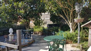 An outdoor patio area with green metal tables and chairs, surrounded by lush greenery and a wooden fence. - Shiralee Holiday Home (Salisbury)
