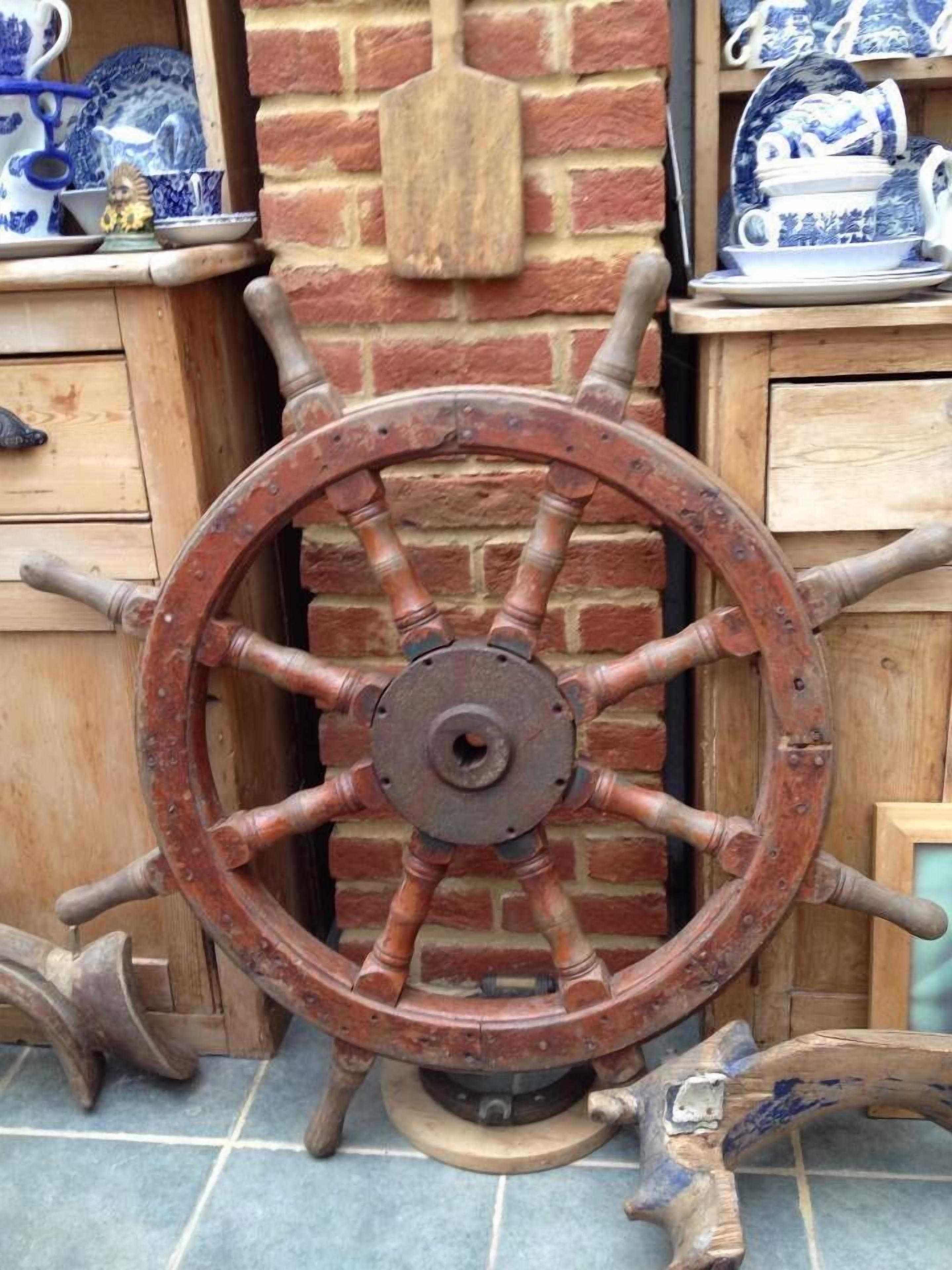 A rustic wooden wheel with a metal hub, set against a brick wall with a wooden cabinet and shelves holding blue and white ceramic items.