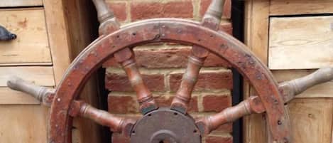 A rustic wooden wheel with a metal hub, set against a brick wall with a wooden cabinet and shelves holding blue and white ceramic items.