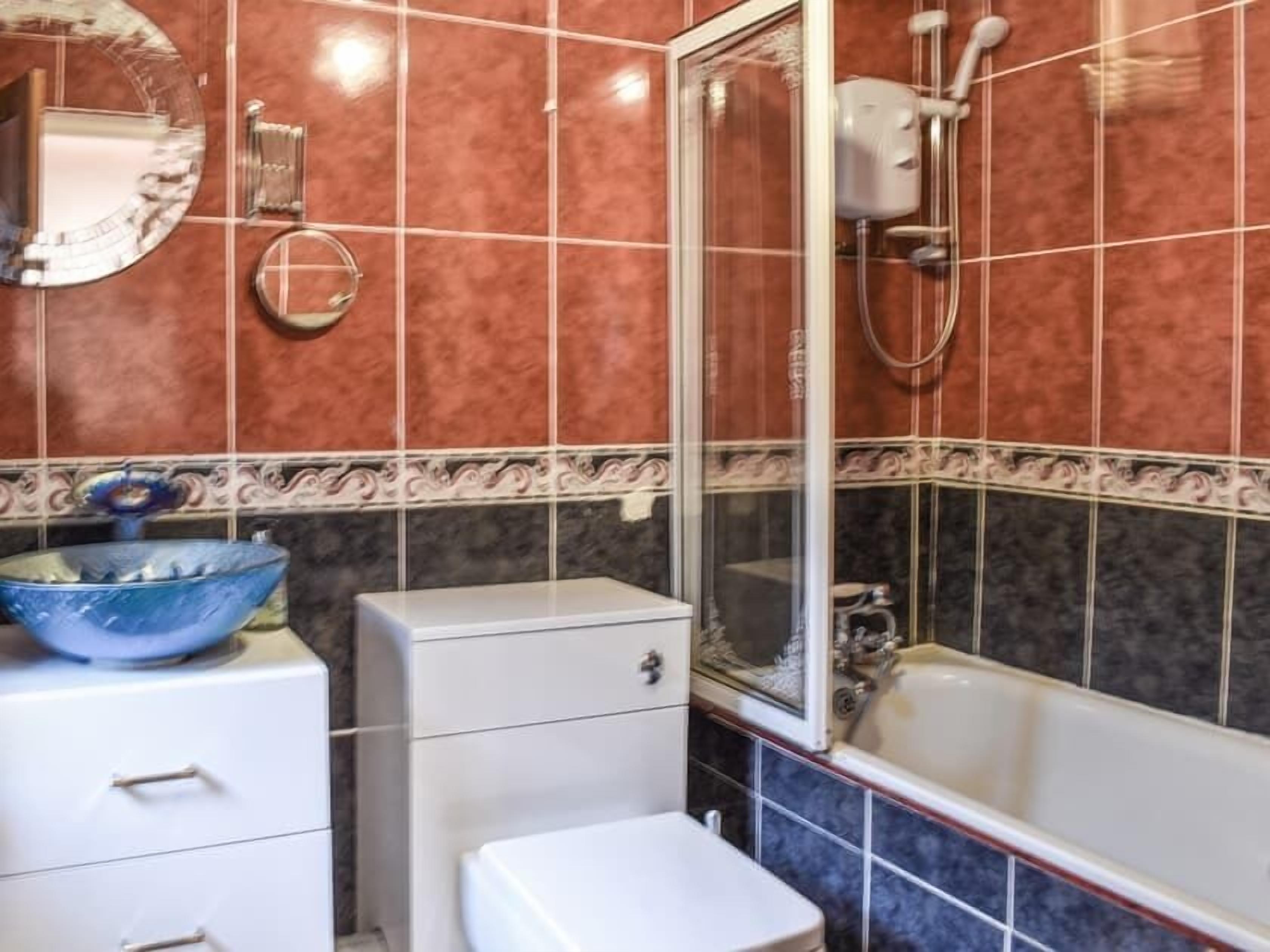A bathroom with a bathtub, a toilet, a sink with a blue bowl, and a mirror.