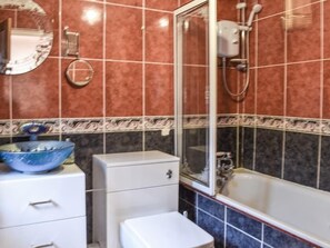 A bathroom with a bathtub, a toilet, a sink with a blue bowl, and a mirror.