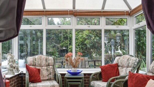 A conservatory with wicker furniture, a blue vase, and a view of greenery outside. - Shiralee Holiday Home (Salisbury)