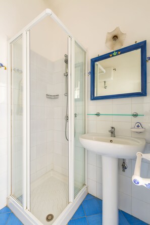 Un bagno con doccia vetrata, un lavandino bianco e uno specchio con cornice blu.
