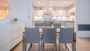 Une cuisine moderne avec des meubles blancs, un îlot central et un coin repas doté de chaises grises.